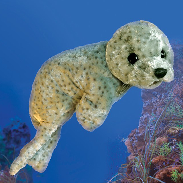 Folkmanis Handpuppe Seerobbenbaby in hellgrauem Fell mit dunklen Flecken, schwarzen Glasaugen und Schnurrhaaren, vor blauem Meereshintergrund