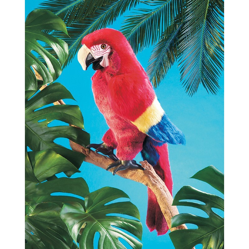 Folkmanis Handpuppe Ara in leuchtendem Rot mit gelb-blauen Flügeln, auf einem Ast sitzend, vor türkisblauem Hintergrund mit Monstera-Blättern