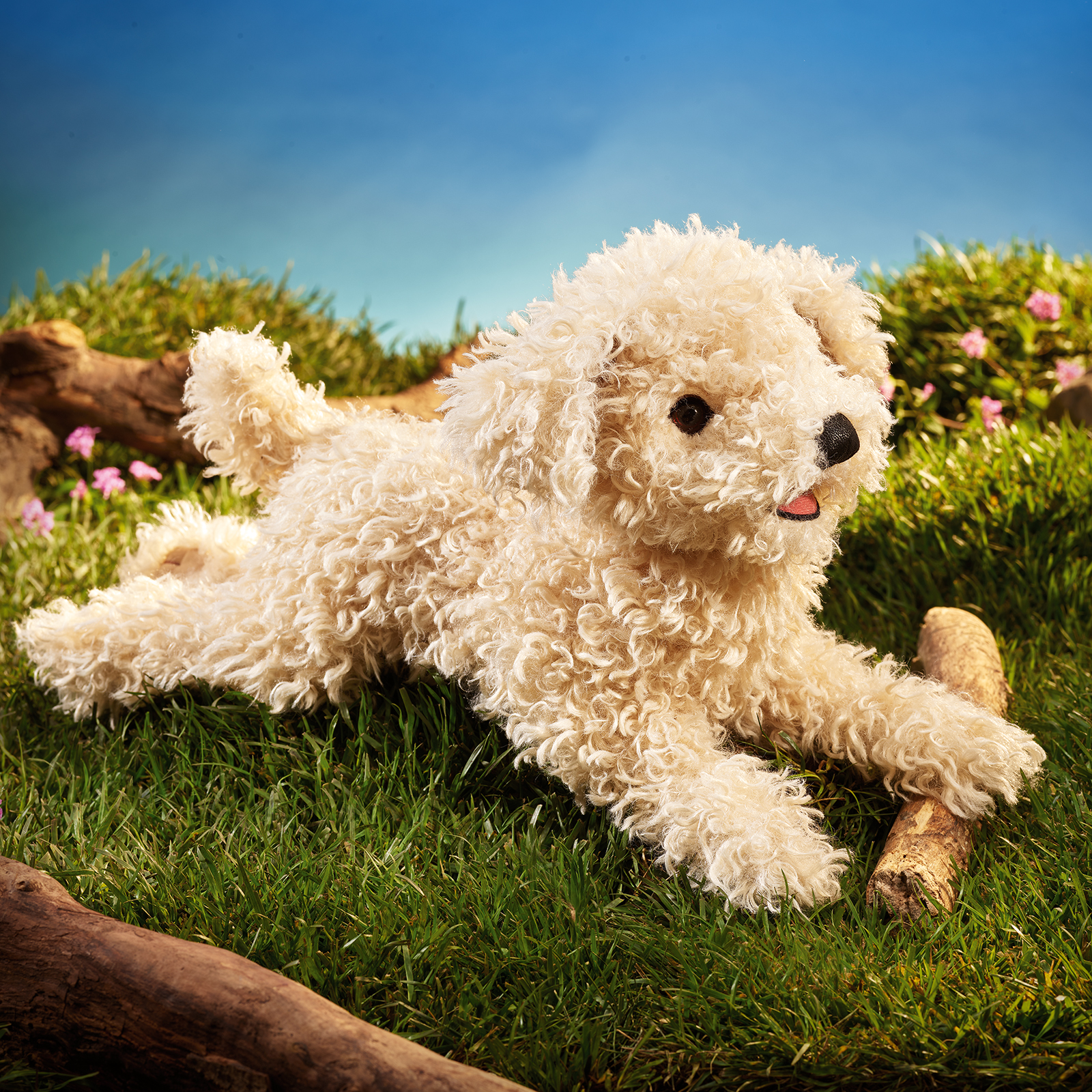 Folkmanis hand puppet white poodle puppy with curly cream-white fur, lying on grass, side view