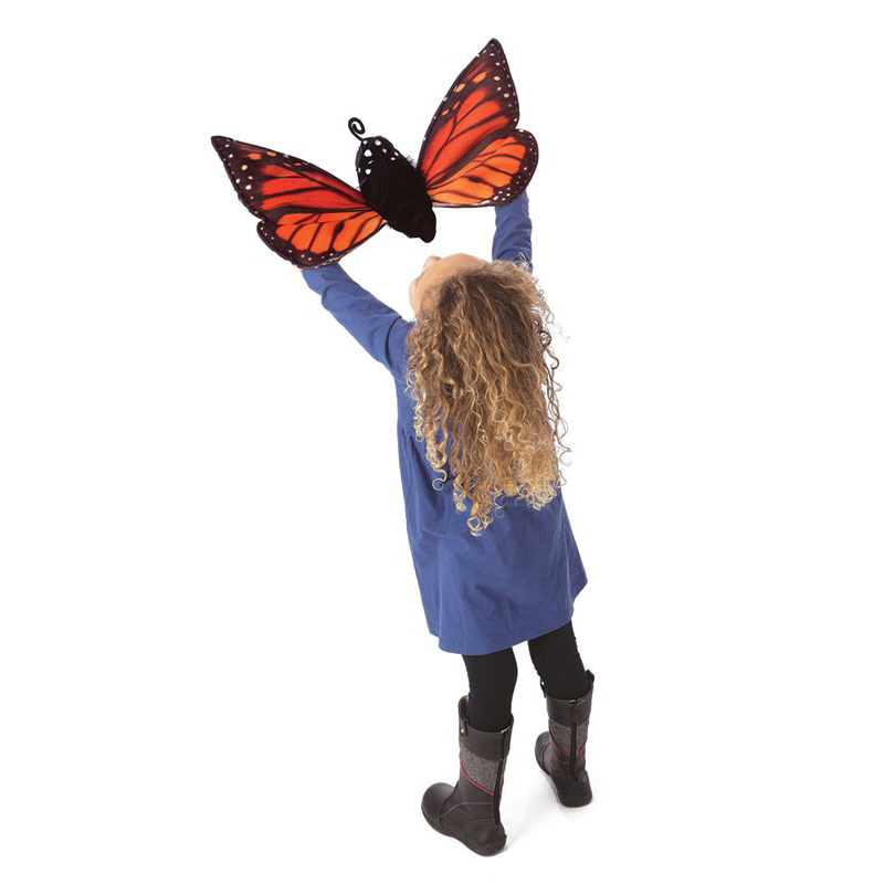 Girl holding a Folkmanis monarch butterfly hand puppet with orange-and-black patterned wings high up in the air