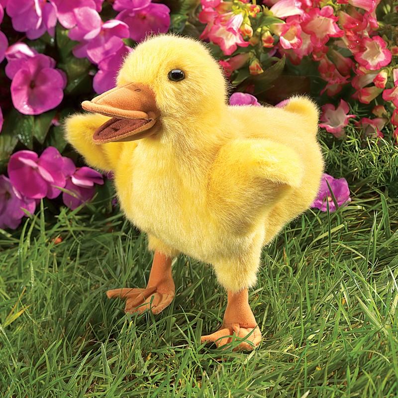 Folkmanis Handpuppe Entchen aus gelbem Plüsch mit geöffnetem Schnabel, stehend auf Gras vor rosa Blüten
