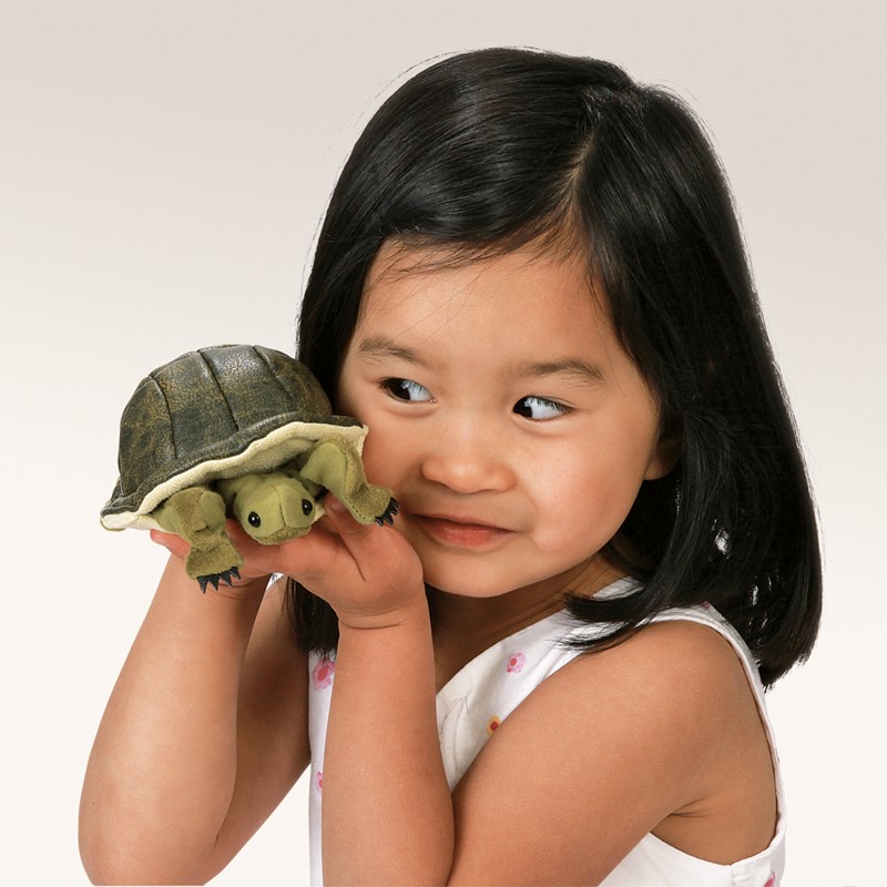 Kleines Mädchen hält Folkmanis Fingerpuppe mini Schildkröte mit dunkelgrünem Panzer auf dem Finger hoch.