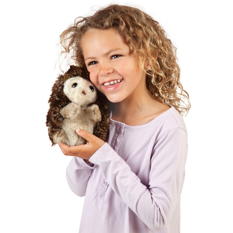 Lächelndes Mädchen hält Folkmanis Handpuppe Igel mit braunem Stachelrücken und hellem Bauchfell in beiden Händen.