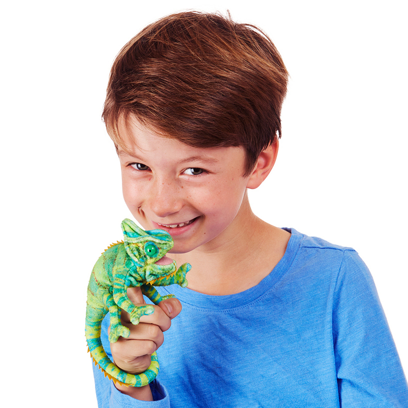 Boy holding a Folkmanis mini chameleon finger puppet in green-turquoise on his finger and smiling at the camera