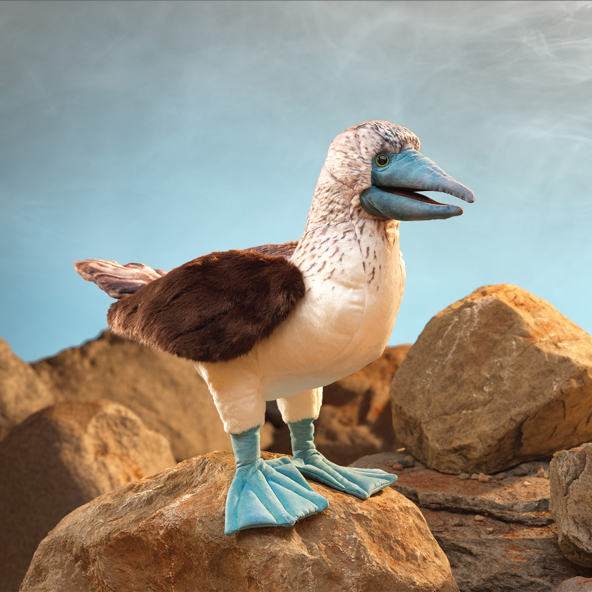 Folkmanis hand puppet blue-footed booby with turquoise webbed feet and blue beak, standing on rocks, side view