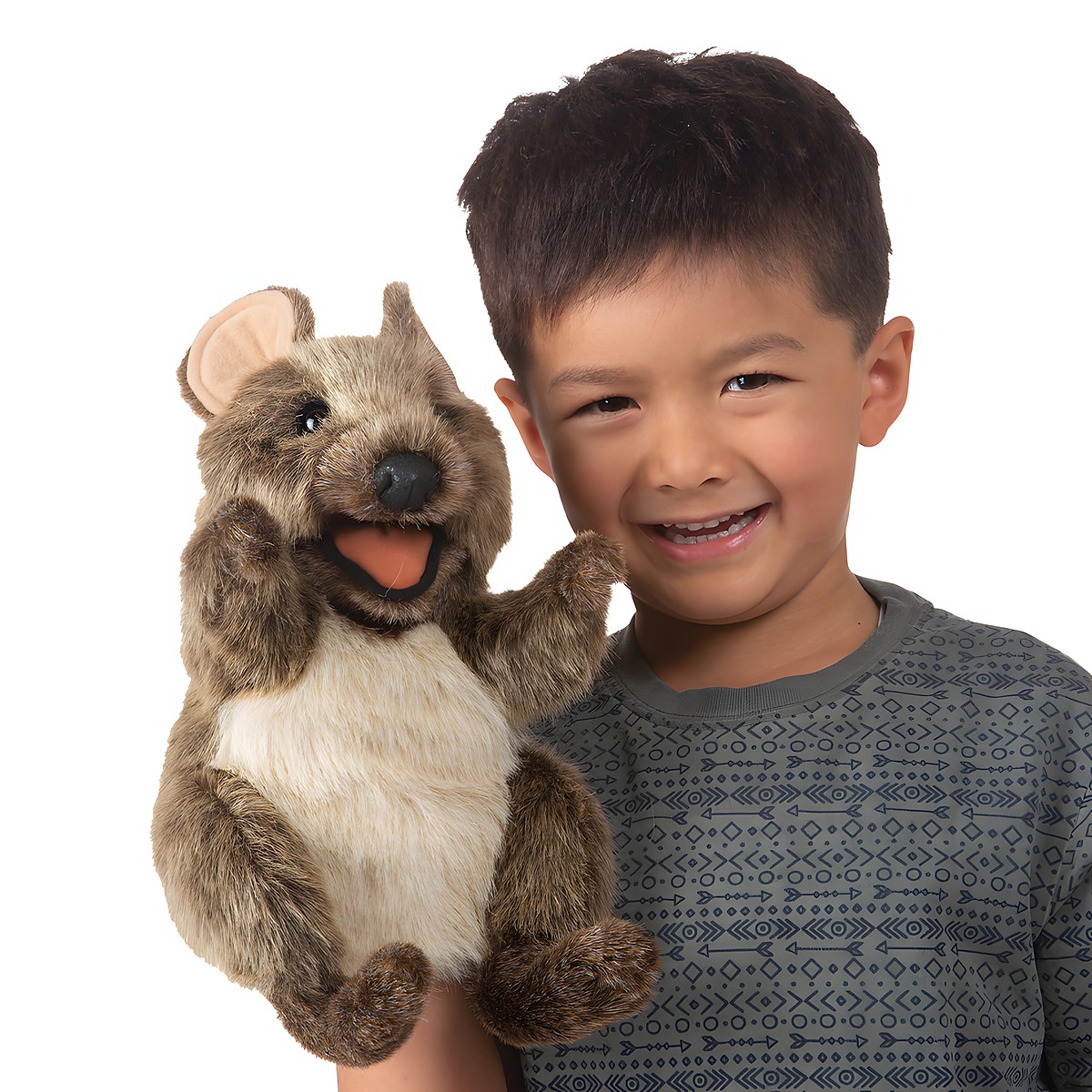 Smiling boy holds up a Folkmanis quokka hand puppet with an open mouth and brown plush fur
