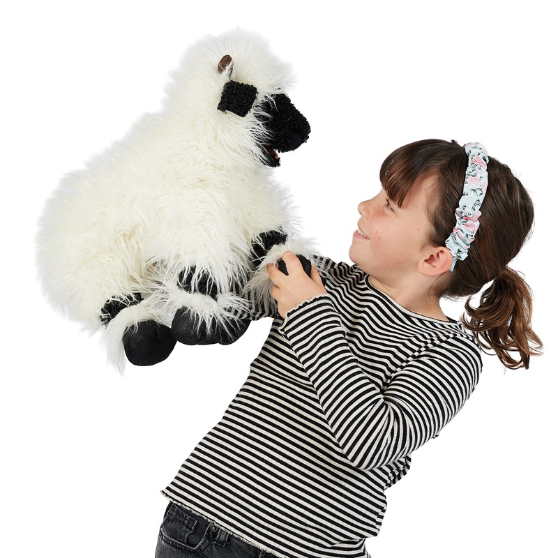 Mädchen hält Folkmanis Handpuppe Walliser Schwarznasenschaf mit weißem Langflor-Fell und schwarzer Gesichtsmaske hoch
