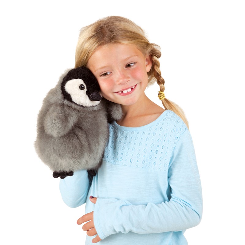 Girl holding a Folkmanis baby emperor penguin hand puppet with grey plush feathers and a white face up to her shoulder