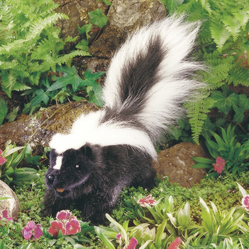 Folkmanis skunk hand puppet with black-and-white fur and a bushy raised tail, side view in a garden setting