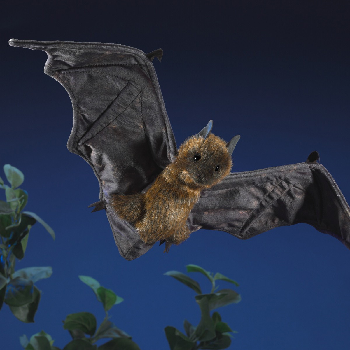 Folkmanis hand puppet flying fox with outstretched dark grey wings and rust-brown fur, posed in flight against a night-blue background