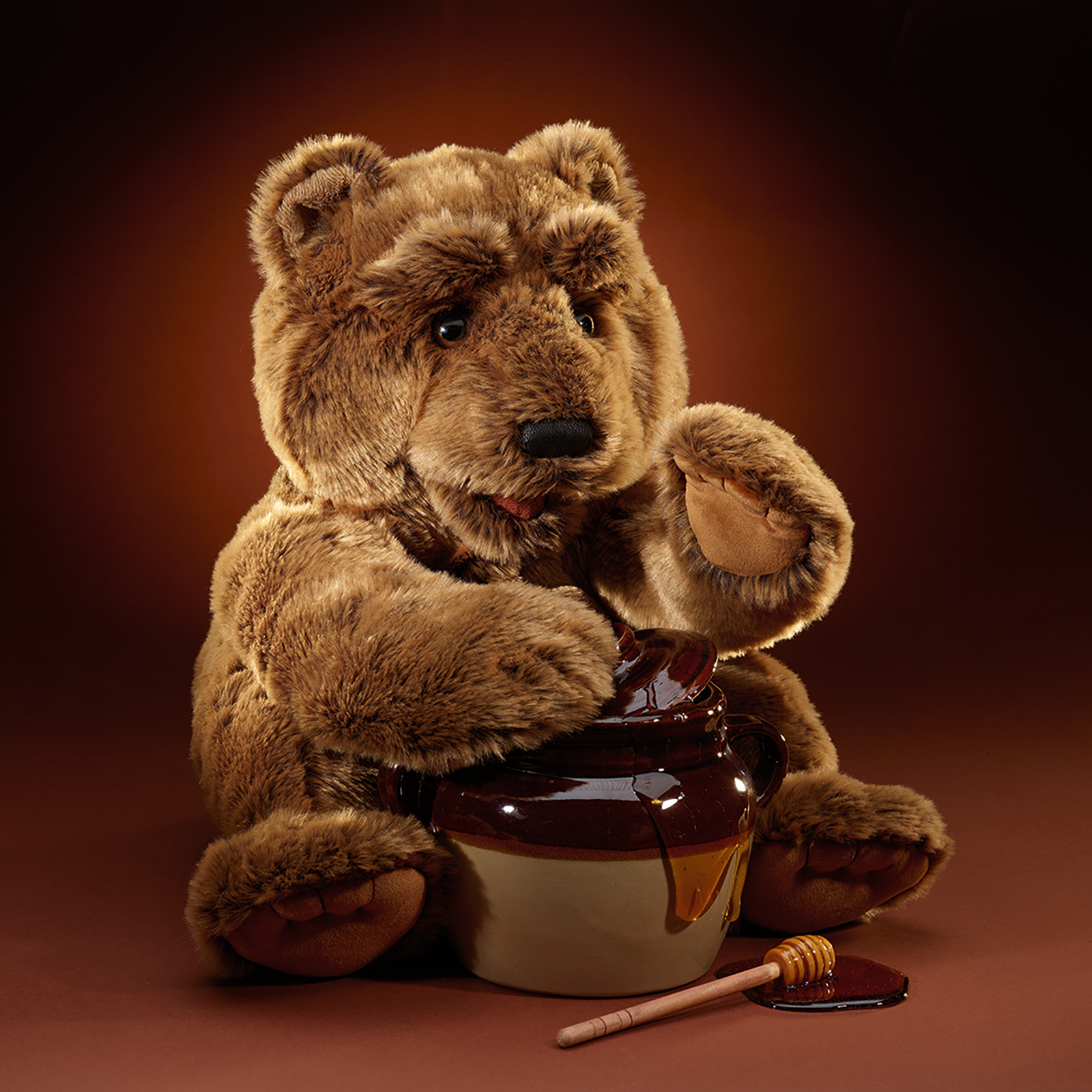Folkmanis Handpuppe großer Bär sitzt vor einem Honigtopf, das Maul geöffnet und eine Pfote danach ausgestreckt.
