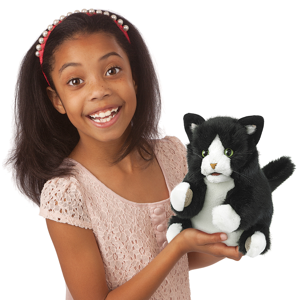 Mädchen hält Folkmanis Handpuppe Tuxedo Kätzchen mit schwarzweißem Fell und grünen Augen in die Kamera