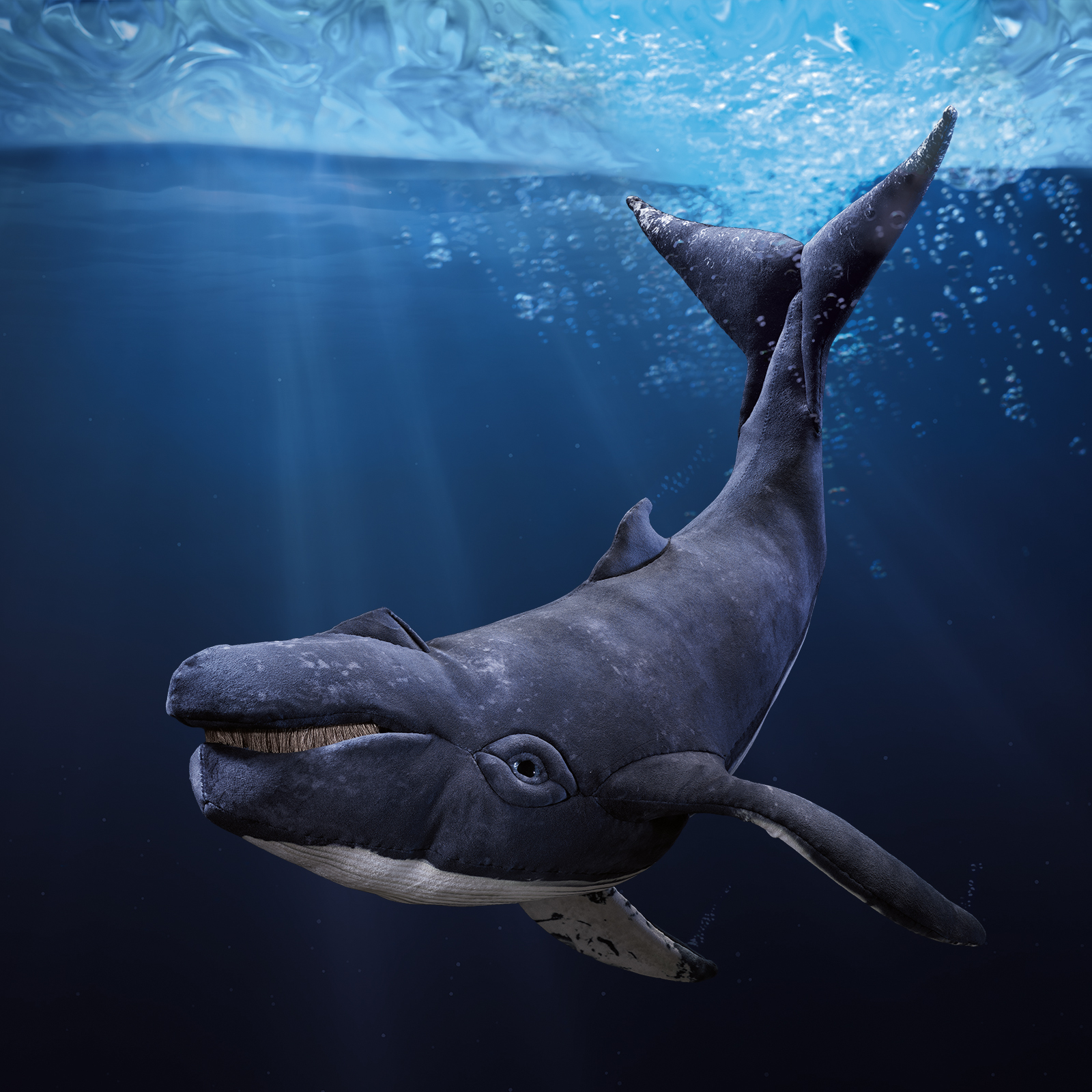 Folkmanis humpback whale hand puppet in dark grey-blue plush, open mouth with baleen plates, side view against an underwater background