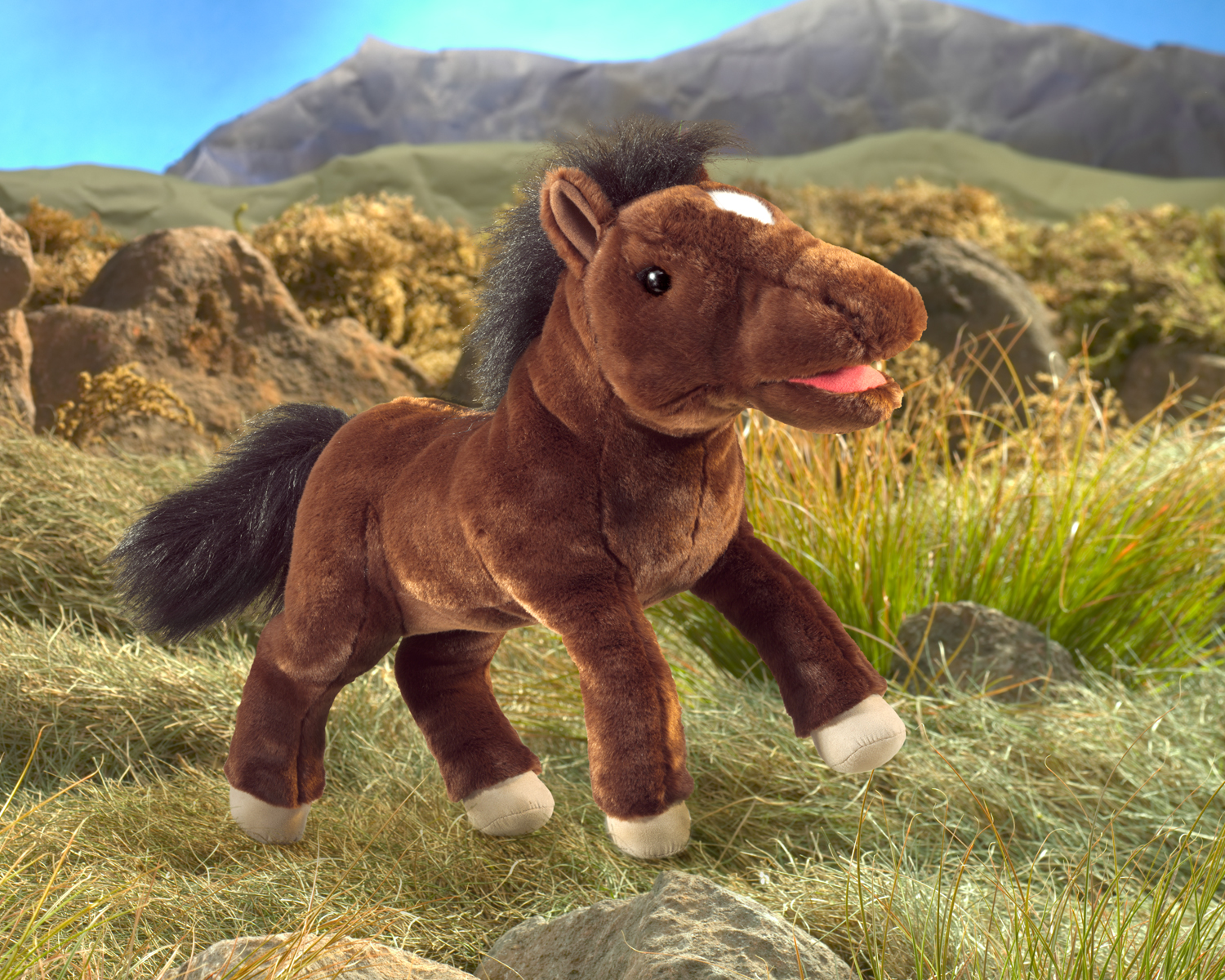 Folkmanis horse hand puppet in dark brown with a black mane, white forehead spot and movable mouth, side view against a mountain backdrop