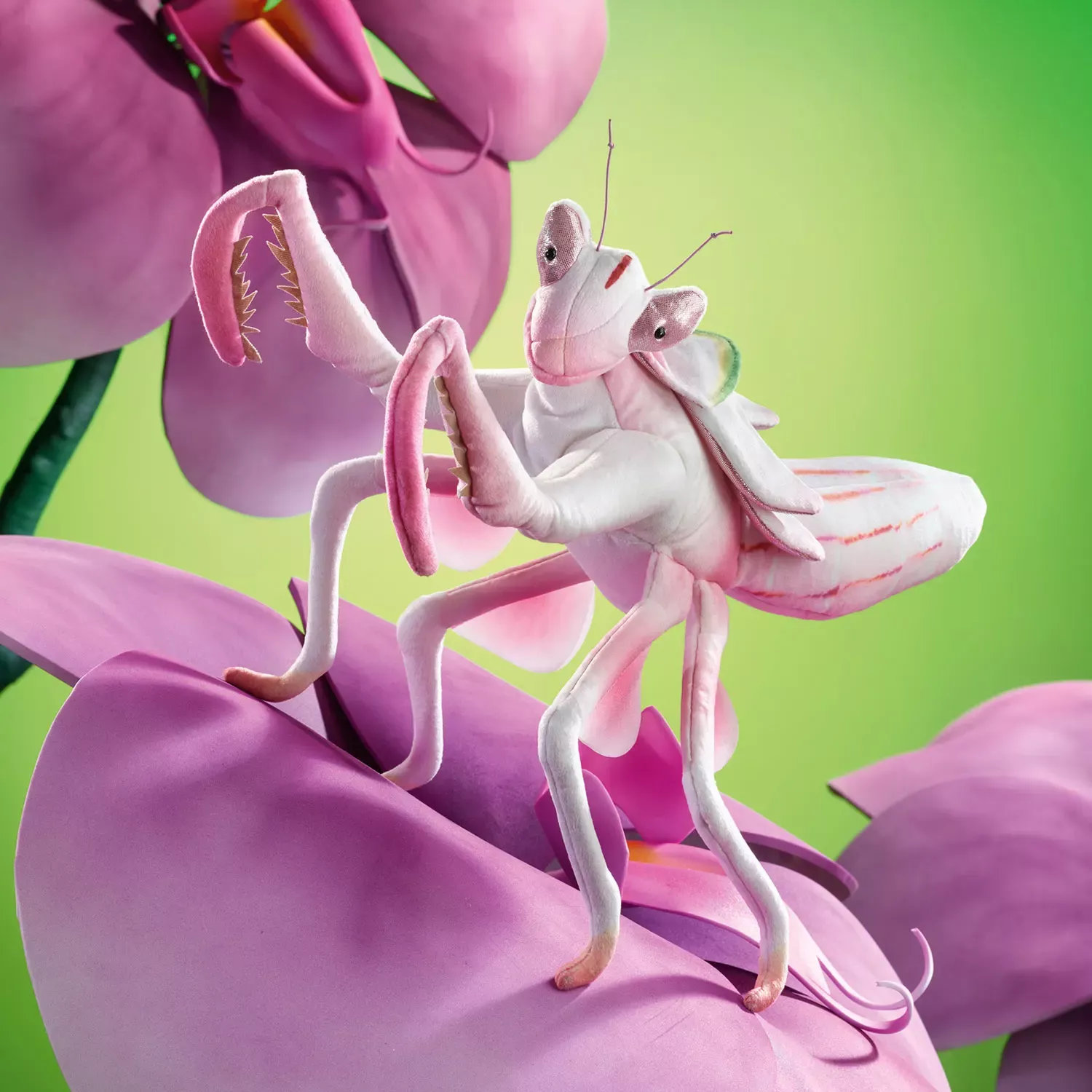 Folkmanis Handpuppe Kronenfangschrecke in Weiß-Rosa mit erhobenen Fangarmen, sitzend auf einer großen pinkfarbenen Orchideenblüte