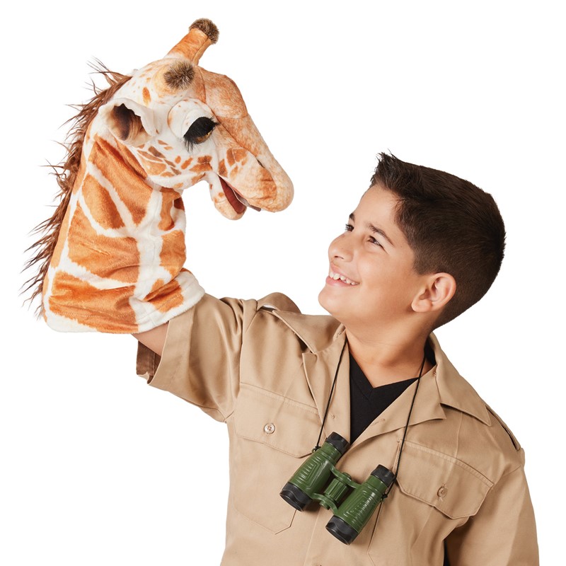 Junge im Safari-Outfit führt die Folkmanis Giraffe Handpuppe mit braun-weißem Fleckenmuster hoch über seinen Kopf.