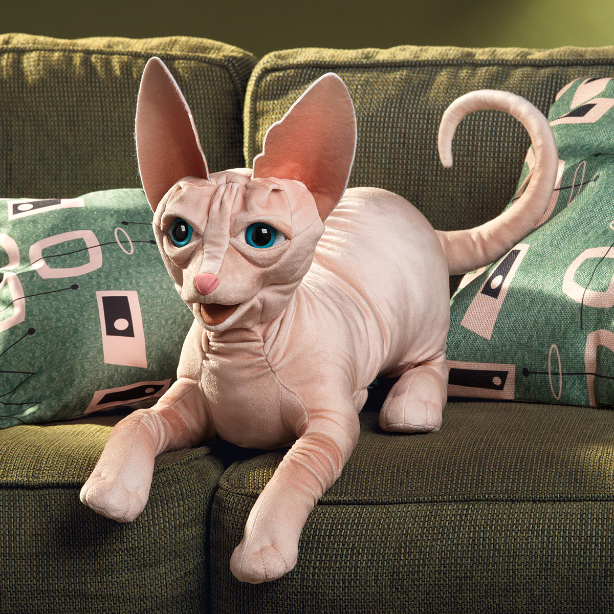 Folkmanis Handpuppe Sphinx Katze in Rosa-Beige mit türkisfarbenen Augen und großen Ohren, liegend auf grünem Sofa