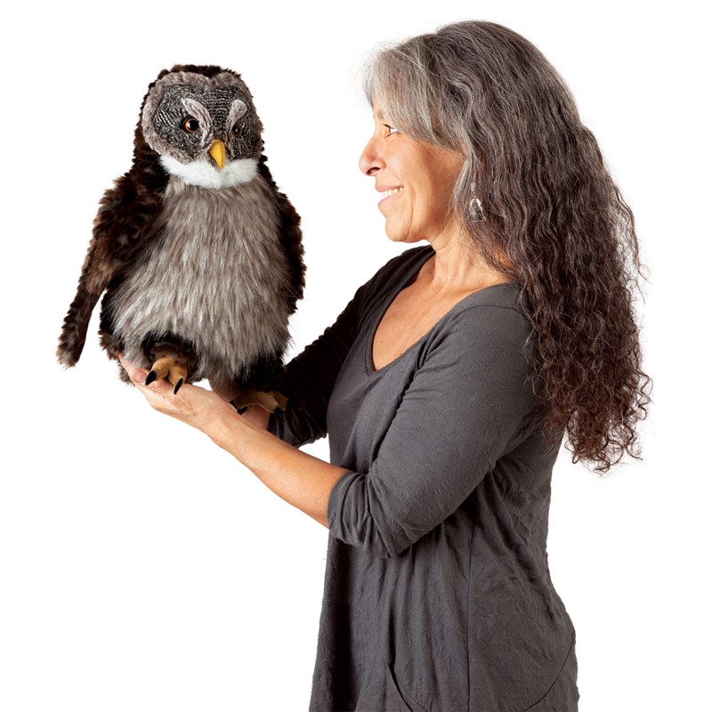 Frau hält Folkmanis Handpuppe Eule mit braunem Gefieder, grauem Bauch und gelbem Schnabel auf der flachen Hand, Seitenansicht.