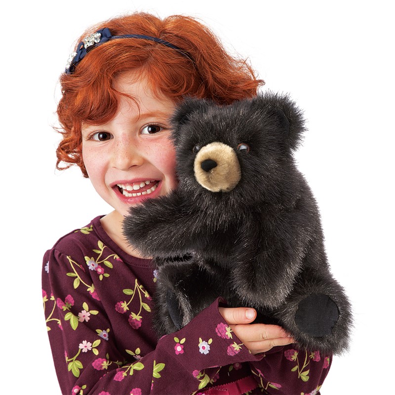 Folkmanis Handpuppe kleiner Schwarzbär mit beigem Schnauzenbereich, schwarzem Fell, von lächelndem Mädchen gehalten