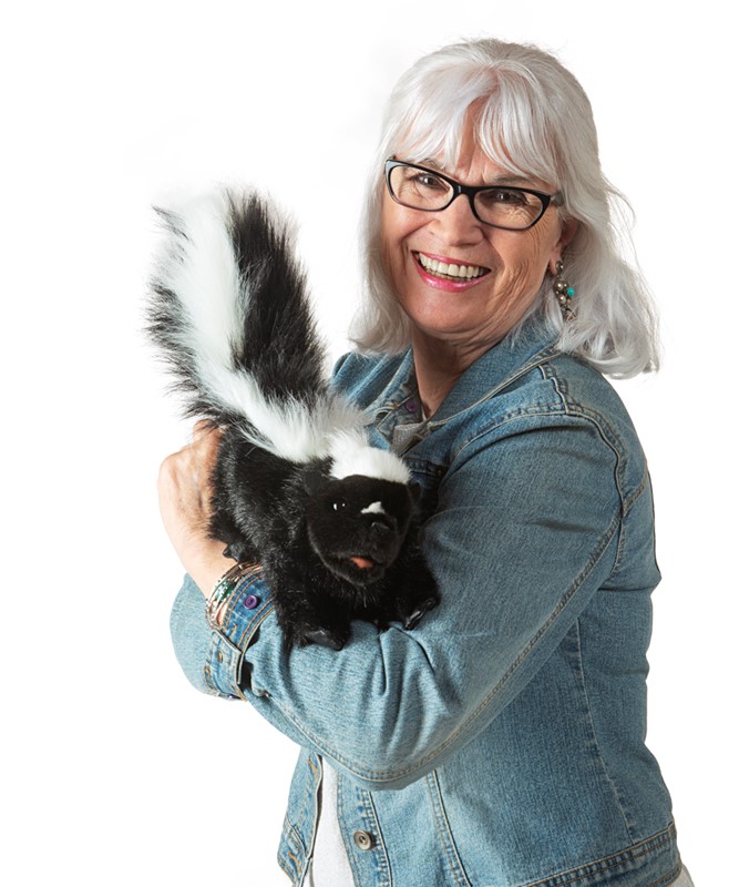 Smiling woman holding the Folkmanis skunk hand puppet with black-and-white fur and a bushy tail in her arms
