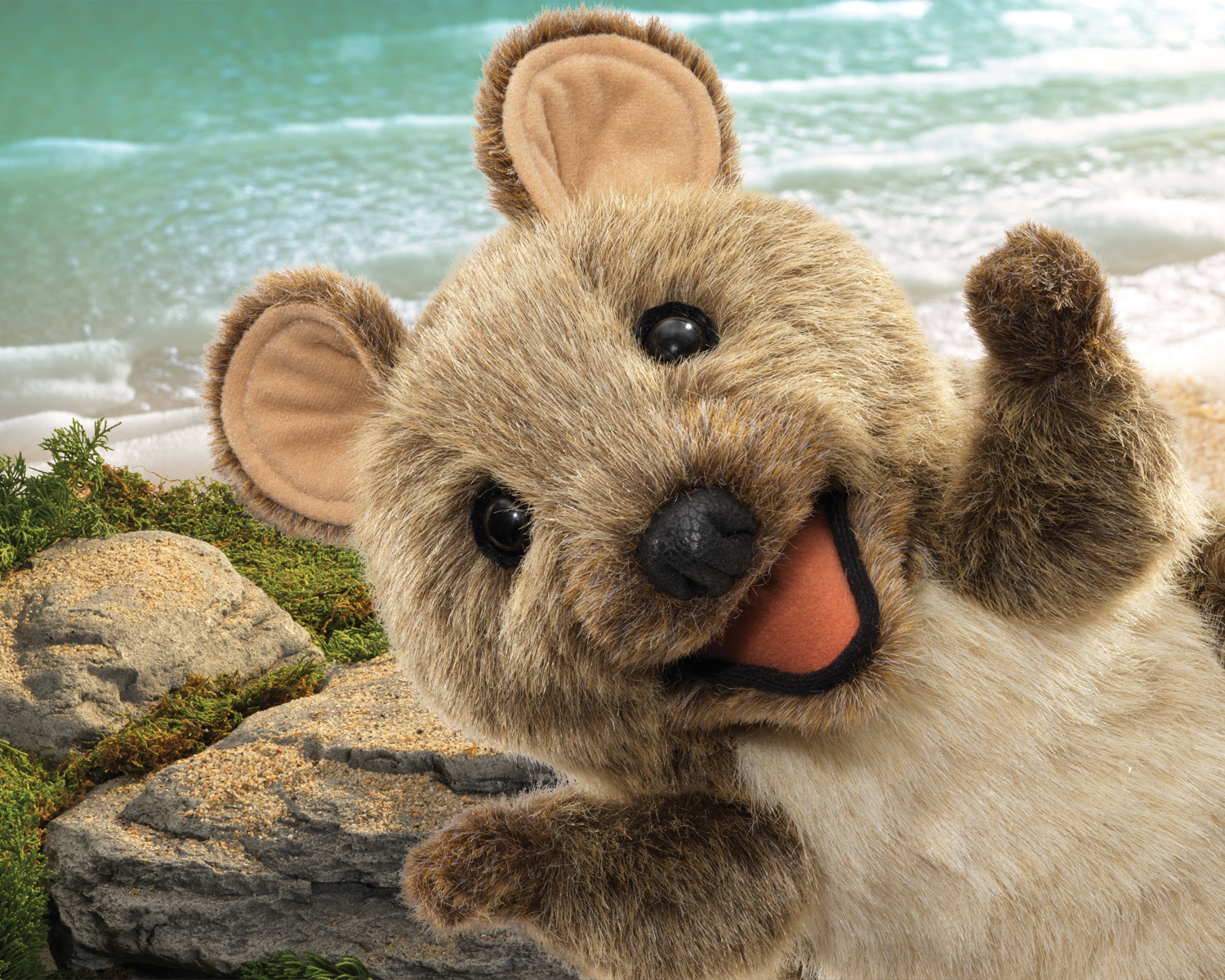 Folkmanis Handpuppe Kurzschwanzkänguru aus braunem Plüsch mit geöffnetem Maul und erhobenem Arm, vor Strand-Hintergrund