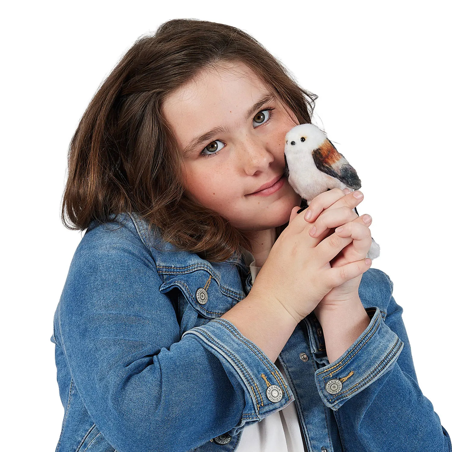 Mädchen hält winzige Folkmanis Fingerpuppe Schwanzmeise mit weißem Gefieder und braunen Flügeln an ihre Wange