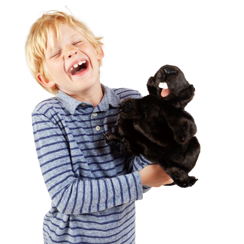 Lachender Junge hält die schwarzbraune Folkmanis Handpuppe Biber mit geöffnetem Maul in den Händen
