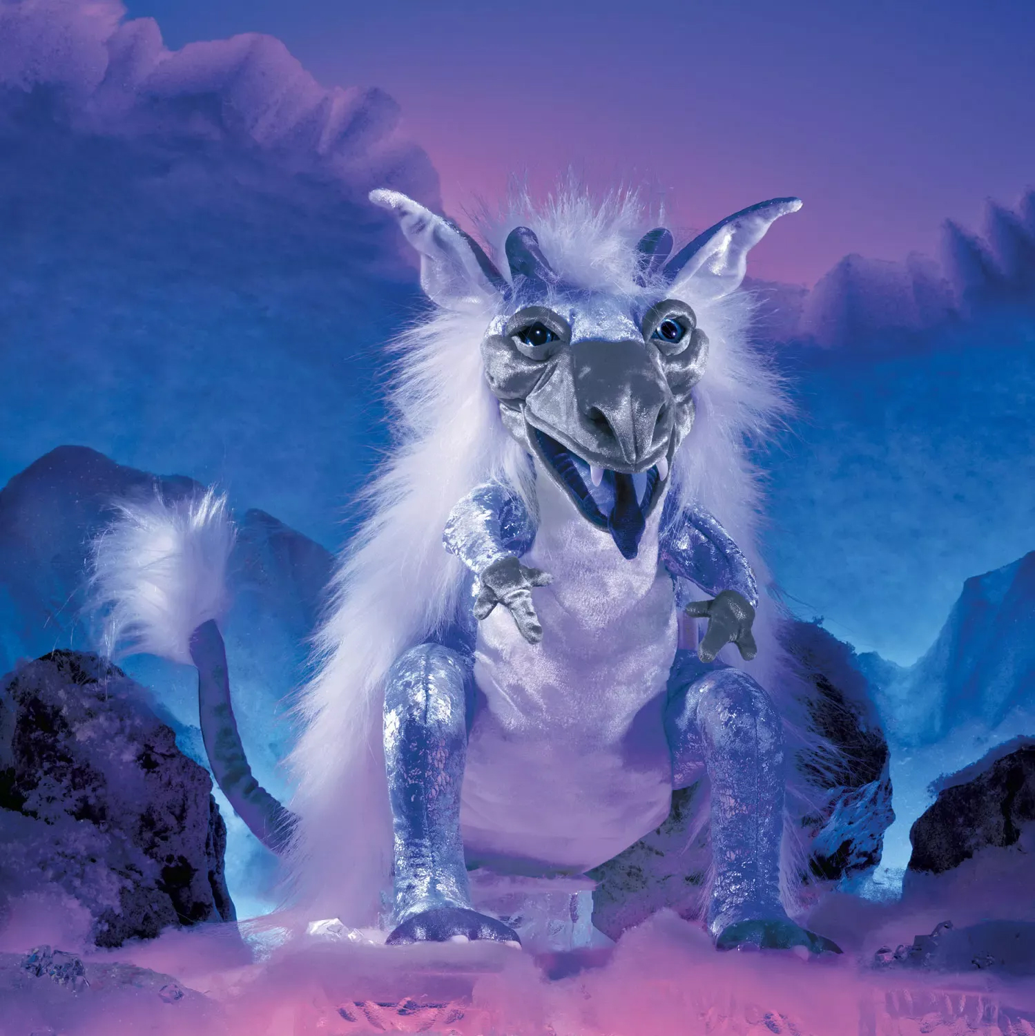 Folkmanis Handpuppe Eisdrache in Silber-Weiß mit geöffnetem Maul, Hörnern und flauschiger Mähne vor eisblauer Bergkulisse