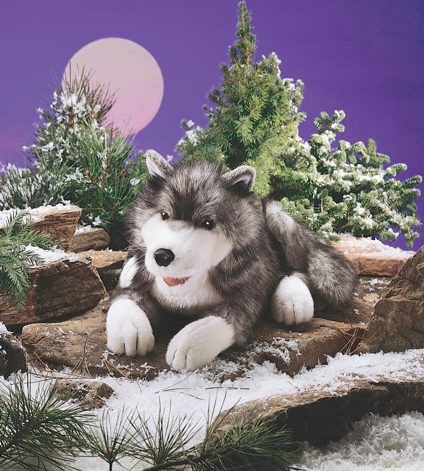 Folkmanis Handpuppe Polarwolf in Grau-Weiß, liegend auf Felsen vor verschneiter Winterkulisse mit Mondscheibe