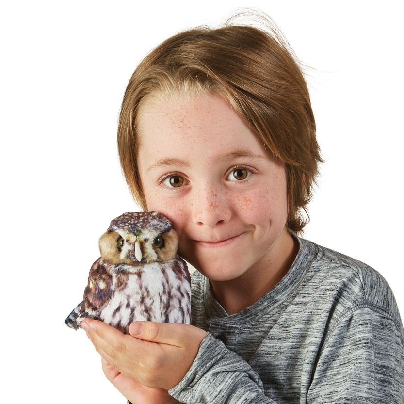Kind hält Folkmanis Handpuppe Sperlingskauz mit braun-weißem Gefieder auf der flachen Hand neben sein Gesicht.