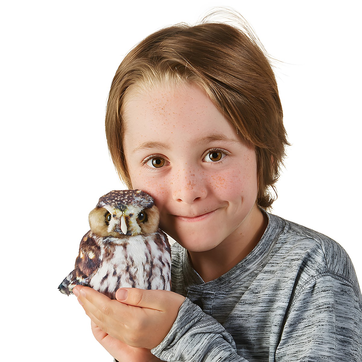 Kind hält Folkmanis Handpuppe Sperlingskauz mit braun-weißem Gefieder auf der flachen Hand neben sein Gesicht.