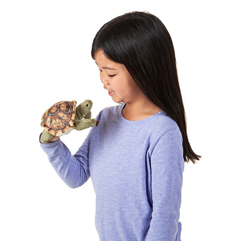 Girl wearing a Folkmanis mini tortoise finger puppet with a patterned shell on her hand, side view
