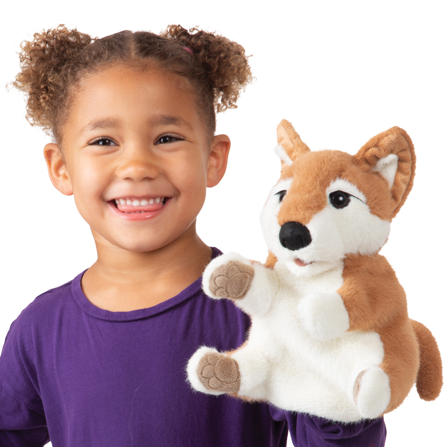Girl holding a Folkmanis Shiba Inu hand puppet with brown-and-white fur and detailed paws up to the camera