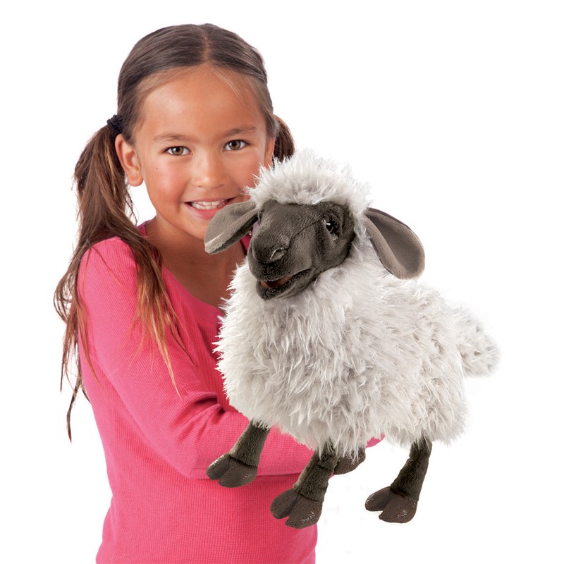 Mädchen hält Folkmanis Handpuppe blökendes Schaf mit weißem Plüschfell, dunklem Gesicht und beweglichem Maul in der Hand.