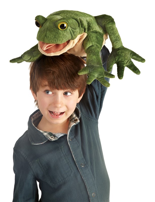 Lachender Junge hält Folkmanis Handpuppe Kröte mit geöffnetem Maul und grüner Strukturoberfläche über seinen Kopf.