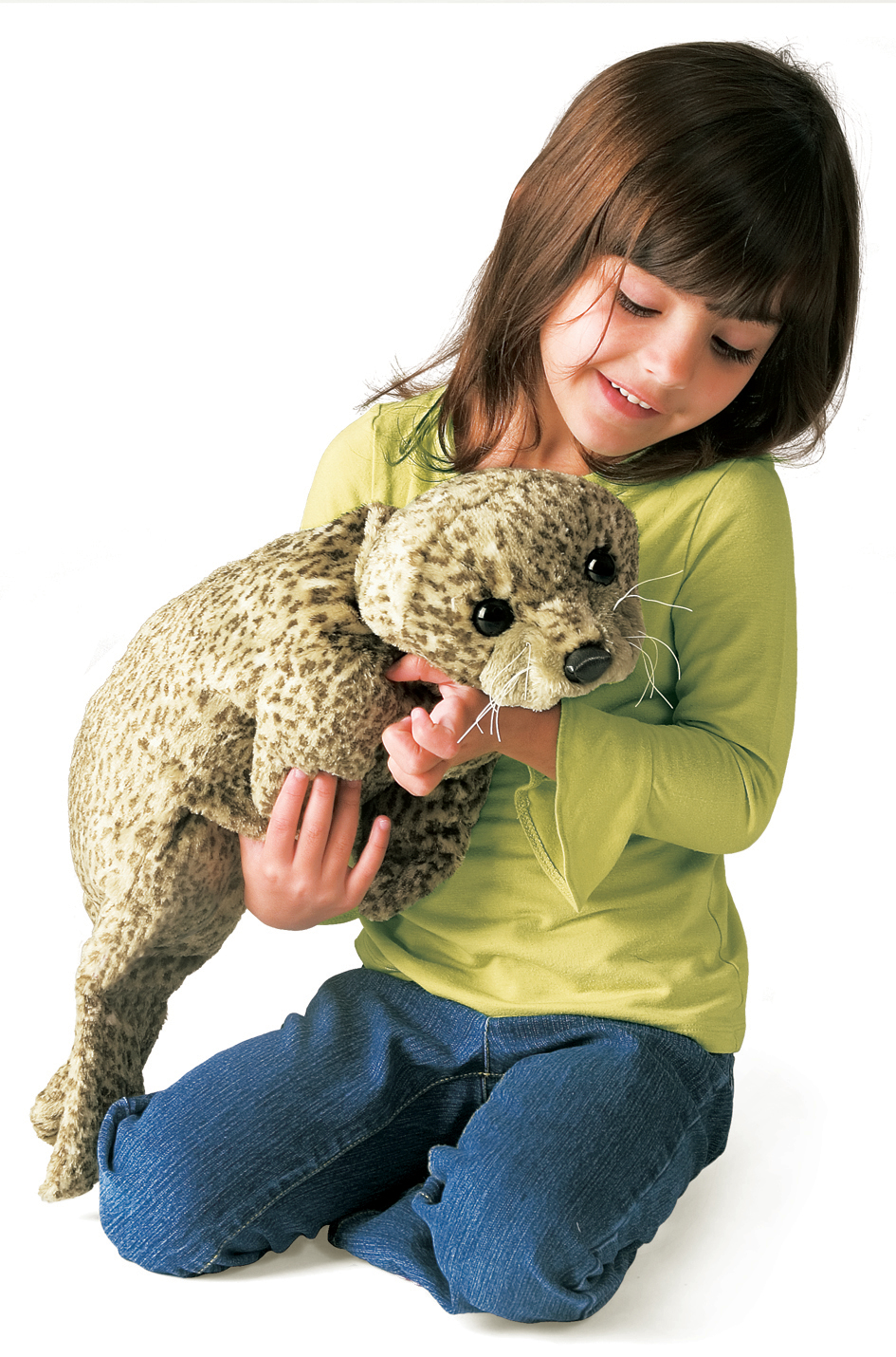 Mädchen hält die Folkmanis Handpuppe Seerobbenbaby mit beiger Fleckenfell-Textur und weißen Schnurrhaaren in beiden Händen.