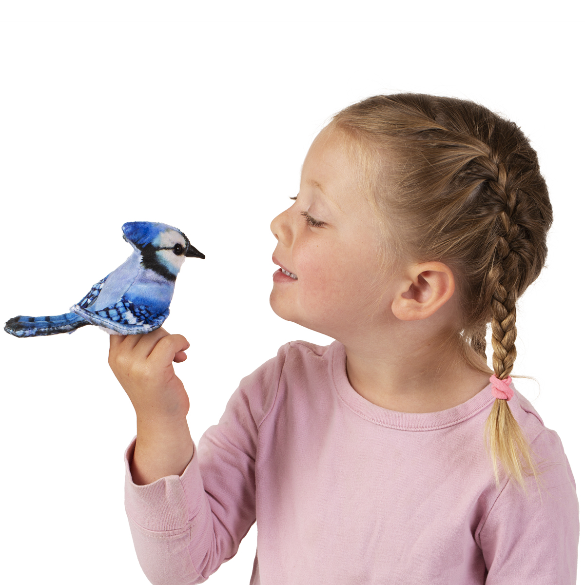 Mädchen hält Folkmanis Fingerpuppe mini Blauhäher mit blau-weißem Gefieder auf dem Zeigefinger und lächelt die Puppe an.