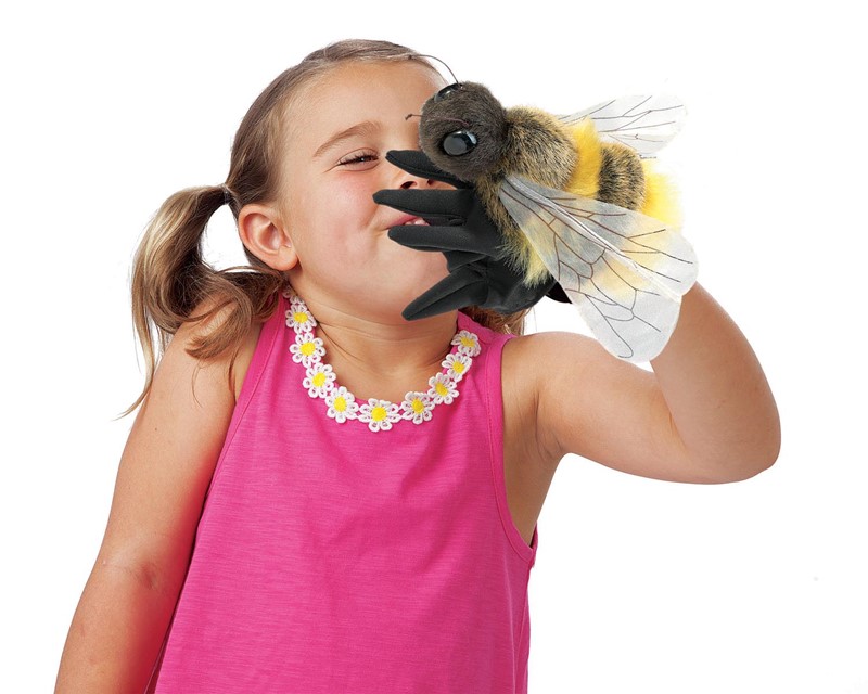 Girl holding a Folkmanis bee hand puppet with a black glove, yellow-black plush body and transparent wings up to her face