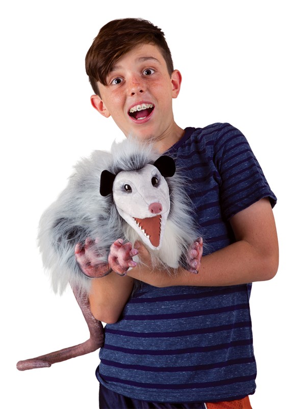 Junge hält Folkmanis Opossum-Handpuppe mit geöffnetem Maul und grau-weißem Zottelfell in den Armen.