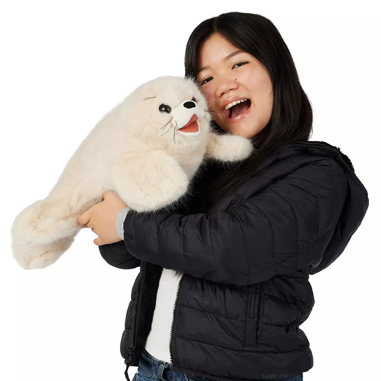 Mädchen hält große Folkmanis Handpuppe Sattelrobben-Baby mit weißem Plüschfell, schwarzen Augen und geöffnetem Maul im Arm.