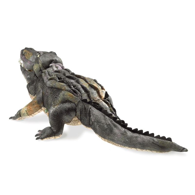 Folkmanis American Alligator hand puppet shown at an angle, with detailed textured scales in dark grey and olive brown, a jagged back ridge, and a long tail
