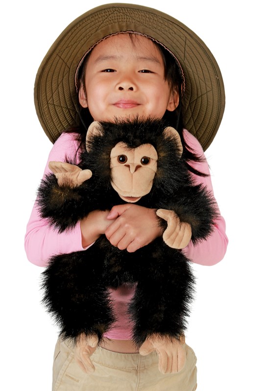 Folkmanis baby chimpanzee hand puppet with black plush fur and beige face, held by a child wearing a safari hat