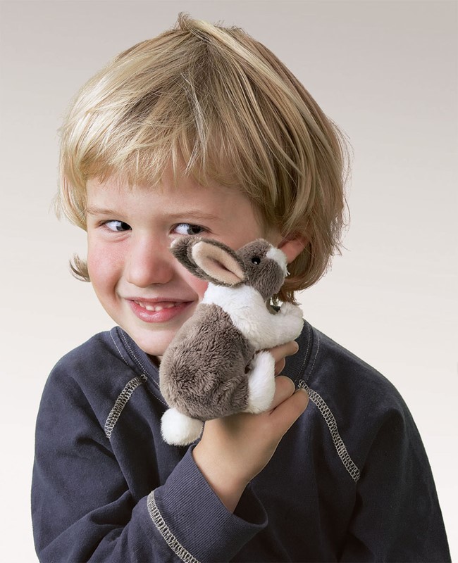 Smiling boy holding a small brown and white Folkmanis mini rabbit finger puppet on his finger