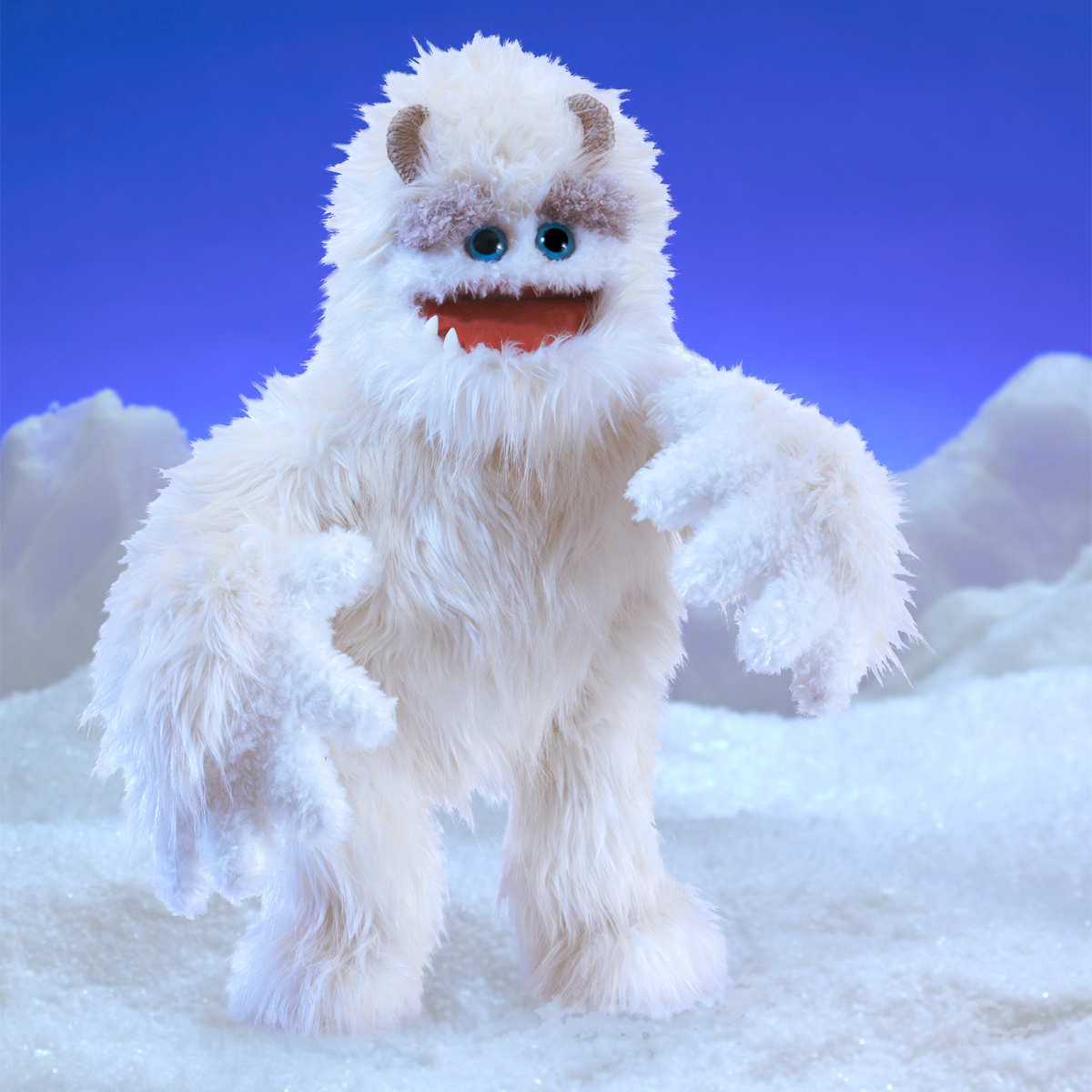 Folkmanis hand puppet yeti with white long fur, blue eyes and open mouth, against a wintry snow backdrop