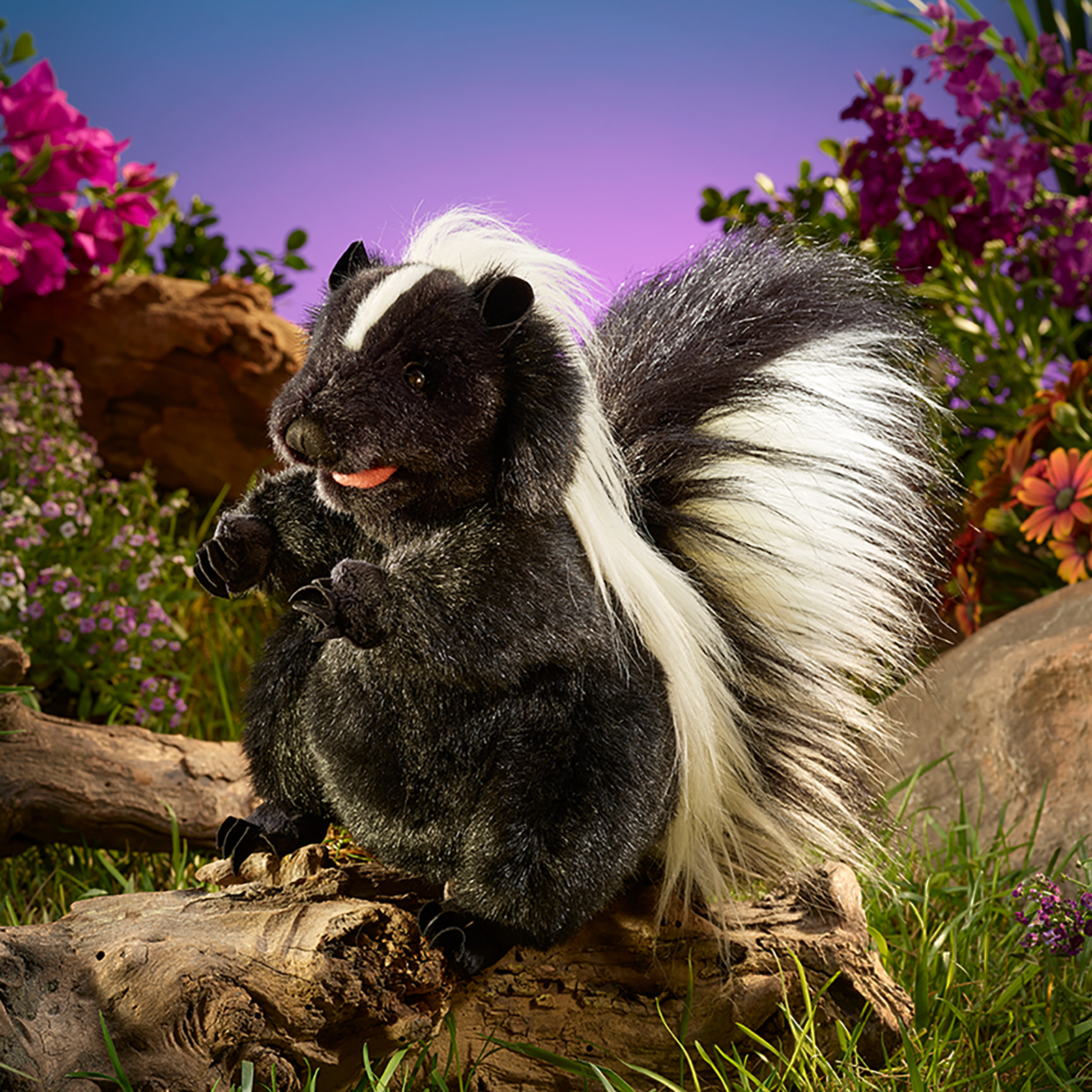 Folkmanis Handpuppe stehendes Stinktier steht auf einem Ast zwischen Blüten, das Maul geöffnet mit Zunge.
