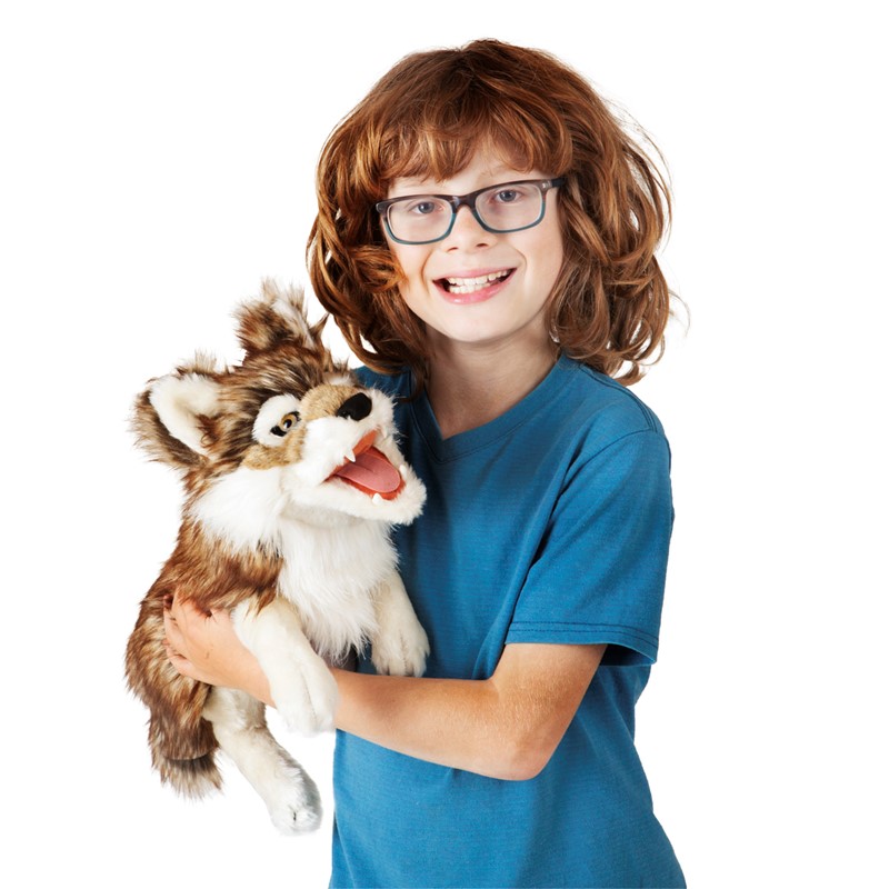 Lachender Junge mit Brille hält die Folkmanis Handpuppe Grauwolf mit geöffnetem Maul und braun-beigem Fell vor weißem Hintergrund.
