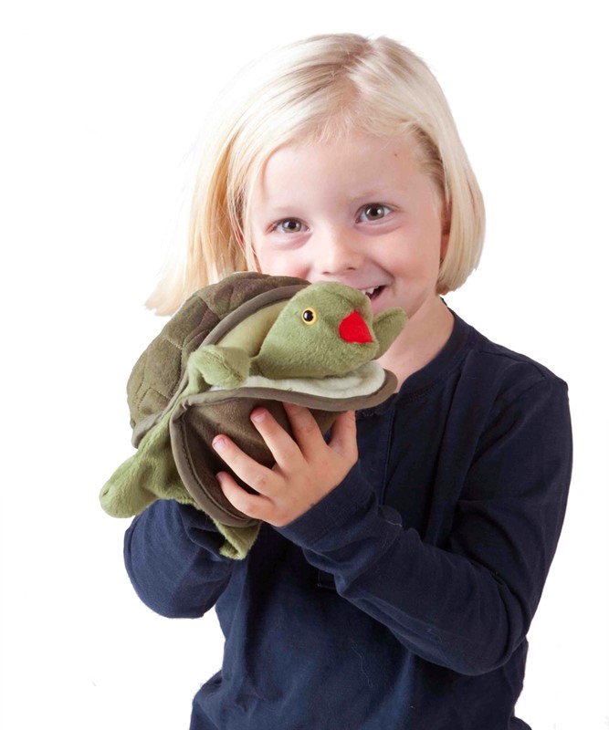 Lächelndes Kind hält die Folkmanis Handpuppe Baby Schildkröte mit grünem Kopf und rotem Maul in beiden Händen.
